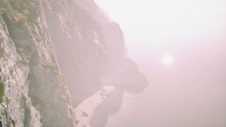 Early morning fog blankets the rugged cliffs as the sun rises gently, casting a soft glow on the peaceful water below and revealing a tranquil landscape at the coast.の写真素材