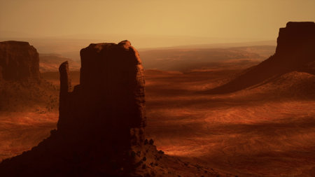 Vast desert scenery showcases towering rock formations against a warm sunset glow. The rugged terrain and deep shadows create a breathtaking view of natures beauty at dusk.の写真素材