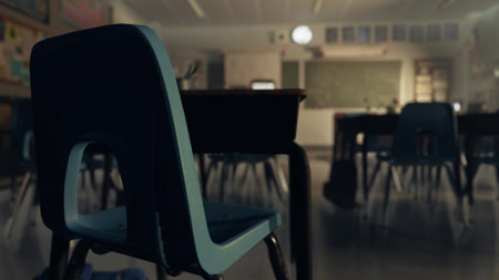 A blue chair is positioned in front of a desk in a quiet classroom. Afternoon sunlight filters in, highlighting the tranquil yet lively atmosphere of learning. The room is ready for students.の写真素材