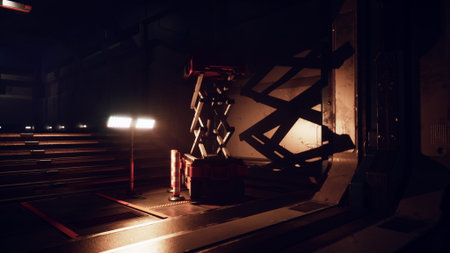 Heavy machinery sits idle in a dimly lit industrial space. A solitary light casts shadows on the walls, creating an atmosphere of quiet anticipation and mystery.の写真素材