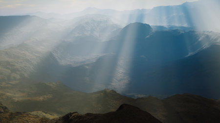 Soft rays of sunlight break through clouds, casting light over a vast mountain range during early morning. The serene beauty creates a peaceful and awe inspiring atmosphere.の写真素材