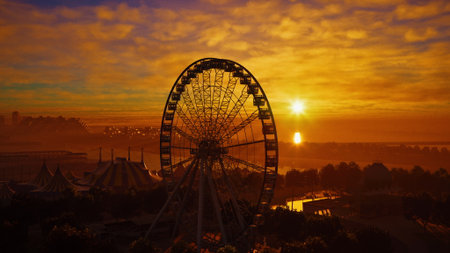 As the sun sets, vibrant colors fill the sky above an amusement park. A towering ferris wheel stands silhouetted against the golden backdrop. Joyful laughter echoes as the day ends.の写真素材