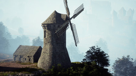 A majestic windmill rises from a lush hillside, surrounded by soft morning mist. The sun gently illuminates the scene, creating a peaceful atmosphere that invites reflection.の写真素材