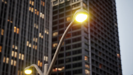 Golden lights from modern street lamps illuminate a bustling urban street, highlighting tall skyscrapers. The ambiance reflects a lively city life at dusk, inviting exploration.の写真素材