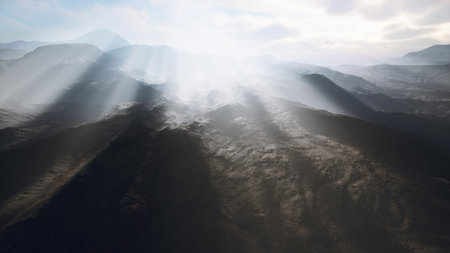 Soft rays of light break through the clouds, casting an ethereal glow over rugged mountains. The interplay of light and shadow highlights the natural beauty at dawn.の写真素材