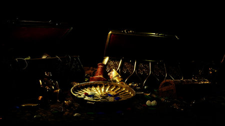 In a dimly lit cave, hidden treasures glimmer from ancient chests. Gold coins, sparkling gems, and mysterious artifacts await discovery by curious explorers. Shadows dance around the treasure trove.の写真素材
