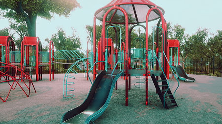 A vibrant playground features bright red and turquoise slides and climbing structures. Trees...