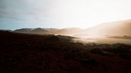 Early morning light casts a warm glow over a tranquil valley. Mist rises from a winding river, while majestic mountains stand tall in the distance, creating a peaceful scene.の写真素材