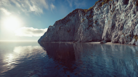 Sunlight casts a soft glow on towering cliffs by the ocean. Calm waters reflect the rocky landscape, creating a serene backdrop for a peaceful moment at dusk.の写真素材