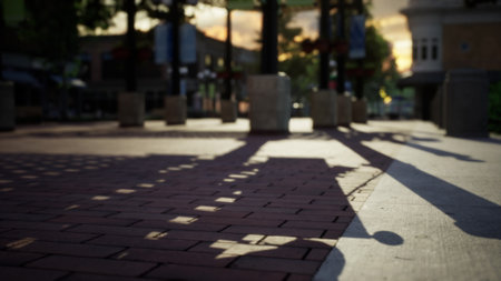Soft shadows stretch over the warm brick stones as the sun sets in the background. The scene captures a peaceful moment in a lively urban area filled with light and tranquility.の写真素材