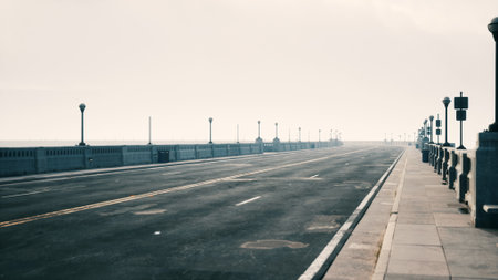 In the early morning, a peaceful seaside bridge stretches into the distance under a soft blanket of fog. Street lamps stand like silent sentinels, adding charm to the serene view.の写真素材