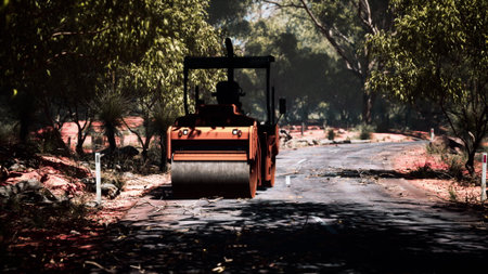 A large road roller is busy smoothing a dusty road in a serene landscape. Tall trees line the path...