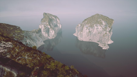 Two impressive rock formations stand tall in a calm lake, surrounded by gentle mist. Morning light softly illuminates the scene, creating a tranquil atmosphere of natures beauty.の写真素材