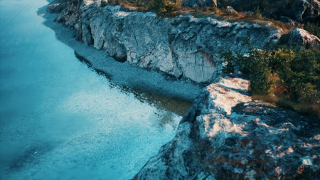 Bright turquoise water laps against a rugged rocky shoreline under a clear sky. Sunlight reflects off the water, highlighting the natural beauty of the landscape.の写真素材