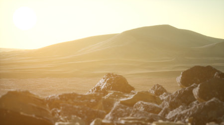 Sunrise casts a warm glow over the endless dunes and rocky terrain of a desert. Soft shadows stretch across the ground, creating a serene atmosphere. The beauty of nature unfolds as day breaks.の写真素材