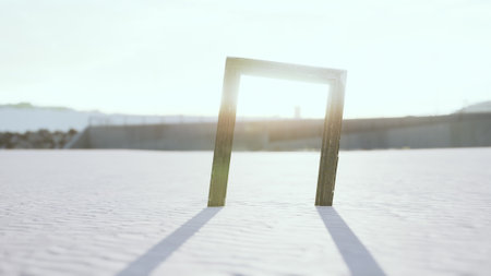 A lone wooden frame rises from the snow, casting long shadows under the warm glow of a winter sun. The serene landscape creates an intriguing contrast with this unusual sight.の写真素材