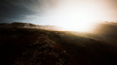 Golden sunlight spills over jagged mountain peaks, casting shadows across a vast, rocky terrain. The tranquil scene invites contemplation and wonder at natures beauty.の写真素材