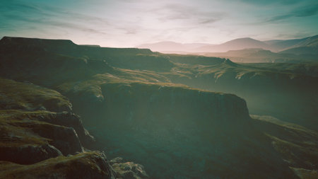 Vast cliffs rise dramatically from the valley floor, bathed in soft morning light. Shadows stretch across the landscape, while distant mountains create a serene backdrop against the clear sky.の写真素材