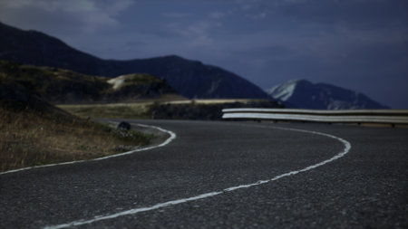 A winding road stretches through rugged mountains, illuminated softly by twilight. The peaceful scene showcases natures beauty and the allure of adventure on an evening drive.の写真素材