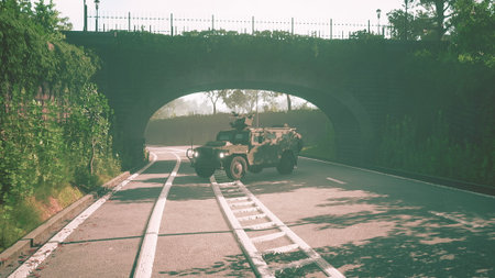 A military vehicle drives along a serene road, passing under an elegant stone bridge surrounded by lush greenery. Sunlight filters through, casting gentle shadows on the asphalt.の写真素材