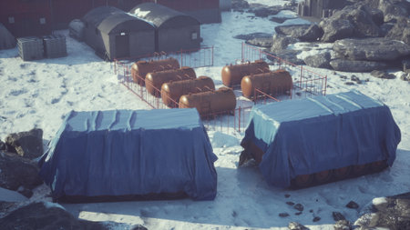 Snow blankets a remote landscape featuring blue tarps covering equipment, surrounded by rocky terrain and a cluster of containers. The quiet beauty of winter captures isolation and resilience.の写真素材