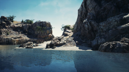 Lush rocky cliffs frame a tranquil cove where crystal clear water meets an empty pebble beach. Sunlight sparkles on the surface while gentle waves lap at the shore, creating a peaceful ambiance.の写真素材