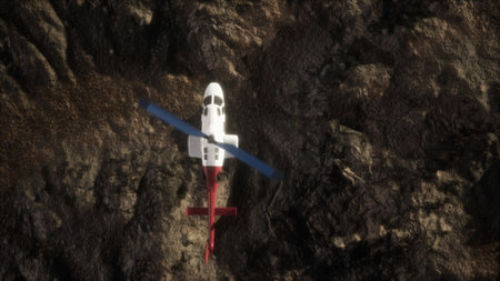 A helicopter is positioned above a rugged landscape, its rotor blades spinning gently. The sun casts light on the rocky ground below, enhancing the texture and depth of the scenery.の写真素材