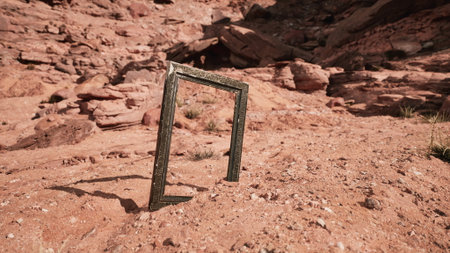 A striking frame rests on the desert floor amidst rugged red rocks and sparse vegetation. The contrasting elements evoke a sense of curiosity and contemplation in the vast landscape.の写真素材