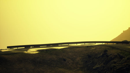 A misty backdrop highlights the gentle curve of the road as it meanders along the hillside. The warm...