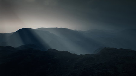 Misty mountain ranges rise dramatically against a twilight sky, with soft rays of light piercing through the clouds, creating a mystical atmosphere in the quiet evening hours.の写真素材