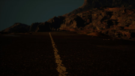 A winding road cuts through rugged rocky landscapes illuminated by twilight. Shadows dance across the surface, creating a mysterious atmosphere as day transitions to night.の写真素材