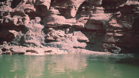 Bright sunlight casts shadows on rugged rock formations as calm green waters gently ripple. Nature surrounds this peaceful canyon, inviting exploration and tranquility amidst stunning scenery.の写真素材