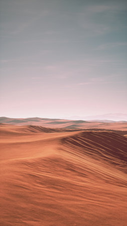 The scene features a vast desert with gentle rolling sand dunes bathed in warm colors. The horizon blends with a soft sky, highlighting the beauty of this arid landscape at dusk.の写真素材