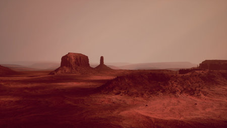 Vast red landscapes stretch under a setting sun, highlighting unique rock formations in the distance. The warm hues create a serene yet awe inspiring atmosphere in the desert.の写真素材