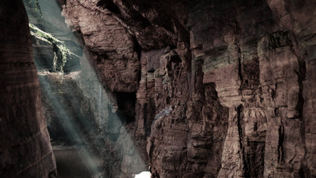 Sunlight streams through a narrow opening in a canyon, creating a magical atmosphere. The rocky walls show textures and shadows, inviting exploration and adventure.の写真素材