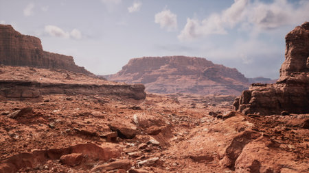 A wide view of a rugged desert landscape features towering rock formations and barren terrain under a bright blue sky. Soft clouds float above, creating a serene atmosphere in this remote location.の写真素材