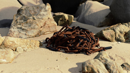 A cluster of rusted chains lies on the sandy surface, surrounded by various rocks.の写真素材