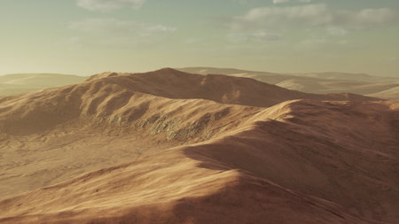 Warm light bathes the undulating hills in a tranquil landscape, creating a serene atmosphere as the sun sets on the horizon. The terrain reveals gentle slopes and distant mountains.の写真素材