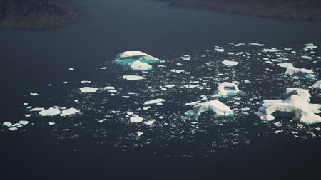 Majestic icebergs float serenely in the Arctic waters, illuminated by sunlight. The deep blue sea...