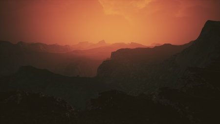 As the sun sets behind rugged peaks, the sky is painted in stunning shades of orange and red, casting a warm glow over the expansive landscape and creating a tranquil ambiance.の写真素材