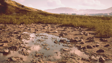 Vibrant hues fill the tranquil landscape, where a small, reflective pool gathers beneath scattered stones. Grassy hills rise in the background, bathed in soft twilight warmth.の写真素材