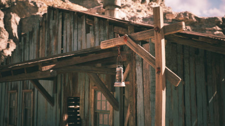 A weathered wooden structure stands in a rugged desert landscape, featuring a lantern hanging from a support beam. The scene captures the charm of old architecture under a bright sky.の写真素材