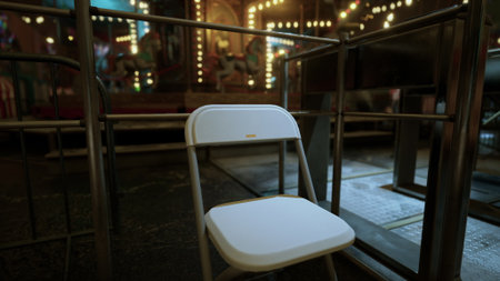 A solitary chair sits in an abandoned amusement park, surrounded by colorful lights that highlight the emptiness of the attractions. The atmosphere is eerie and still.の写真素材
