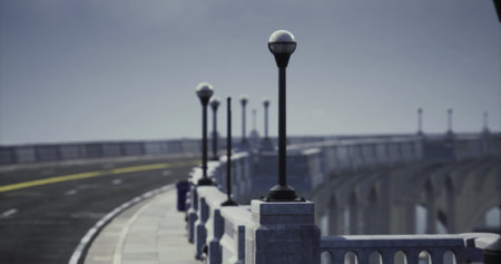A scenic view of a beautifully designed bridge is highlighted by elegant lampposts along the edge. The winding road stretches into the distance, set against a soft, morning sky.の写真素材