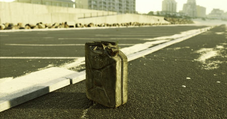 An abandoned fuel canister sits alone on a deserted urban road, surrounded by a barren landscape and distant buildings. The scene conveys a sense of neglect and desolation.の写真素材