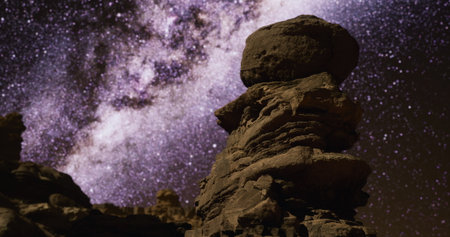 A vivid display of a rock formation stands tall against a beautifully lit night sky filled with countless stars. The Milky Way stretches across the background, creating a mesmerizing sight.の写真素材