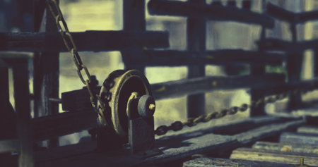 A well worn pulley hangs from a sturdy chain, surrounded by aged wooden beams under soft lighting. This setting evokes a sense of history and craftsmanship in an industrial environment.の写真素材