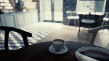 A cup of coffee sits on top of a wooden table in a modern cafe interior.の写真素材