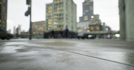A bustling city street is captured from a low angle, with blurred figures walking past modern buildings under a cloudy sky, showcasing urban life and architecture.の写真素材