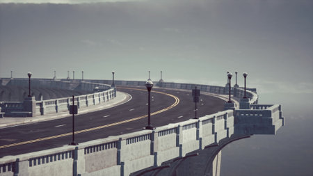 A long, winding road stretches over serene water under a soft, foggy sky. Streetlights line the edges, adding a touch of charm to the peaceful scene, perfect for a quiet journey.の写真素材